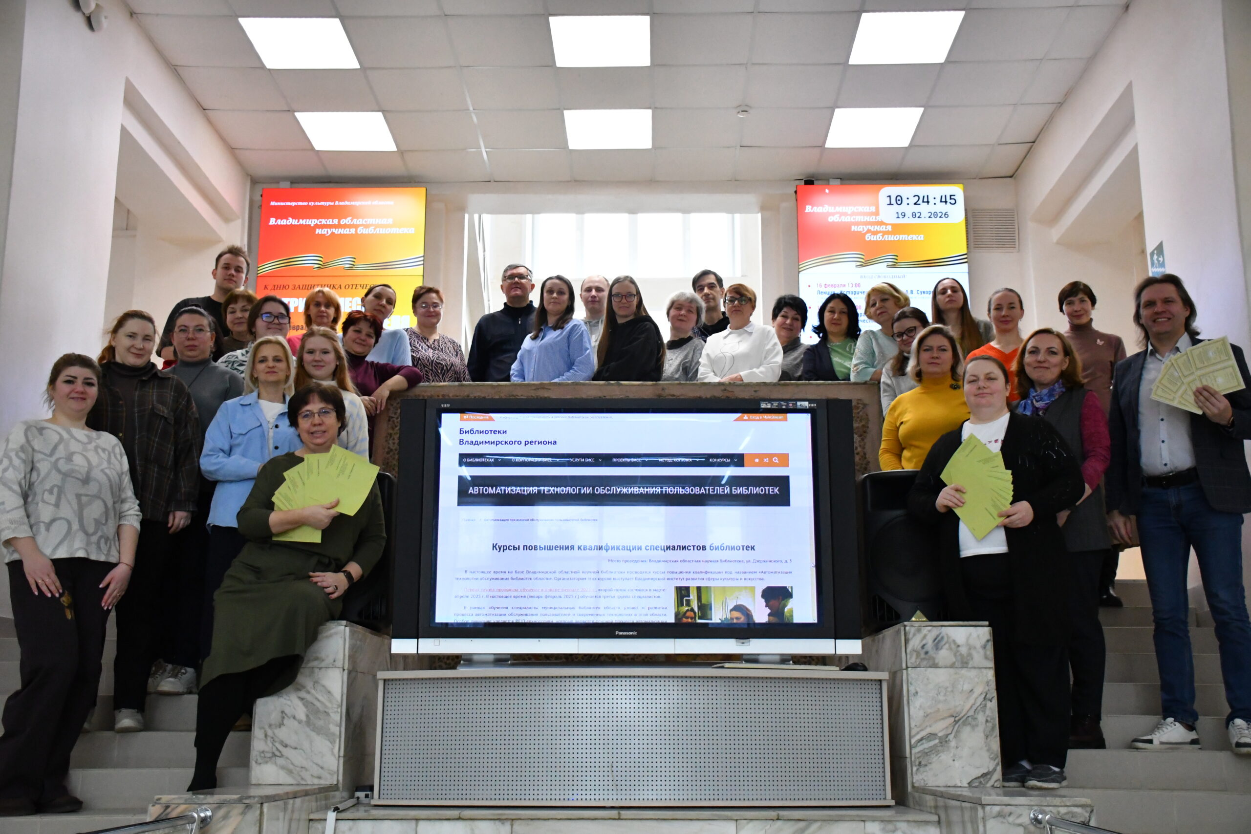 Группа курсантов с преподавателями на лестнице около большого экрана