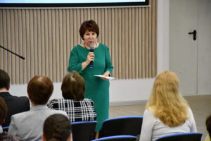 Директор Владимирской областной научной библиотеки на фоне заставки совещания директоров с микрофоном в руке перед аудиторией